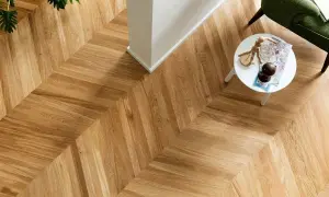 Un elegante parquet a spina di pesce, con un tavolino bianco e una poltrona verde. Per mantenere la sua bellezza, chiediti ogni quanto lavare il parquet.
