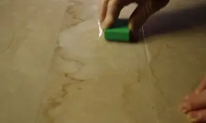 Mano che lucida un marmo corroso con una spugna verde.