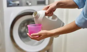 Mani versano candeggina in un misurino rosa, vicino a una lavatrice. Quanto tempo ammollo candeggina?