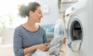 Donna sorridente carica la lavatrice, con un cesto di panni. La scena ricorda una tabella colori lavatrice per la varietà di tessuti.