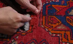 Mani che riparano un tappeto scolorito con ago e filo, un rimedio per ridare vita ai colori sbiaditi.