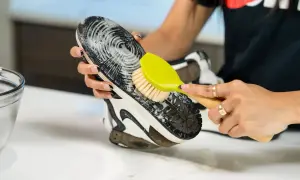 Mani che puliscono la suola di una scarpa con una spazzola, mostrando come pulire le scarpe senza lavarle.
