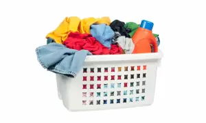 Cesto bianco pieno di panni colorati, con una bottiglia di detersivo arancione. Pronto per il bucato con perborato di sodio.
