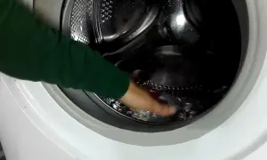 Mano che tocca l'acqua residua nel cestello della lavatrice, un passo per capire come togliere l'acqua dalla lavatrice.