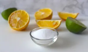 Ciotolina di acido citrico cristallino circondata da spicchi di limone e lime, ingredienti freschi per un tocco frizzante.
