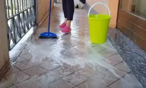 Pulizia del terrazzo esterno: una scopa blu lava le piastrelle con acqua saponata, accanto un secchio giallo.