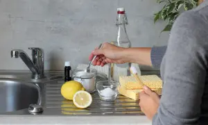 Mano che preleva bicarbonato da un barattolo, con limone, percarbonato e spugne. Differenza tra percarbonato e bicarbonato per pulizie ecologiche.