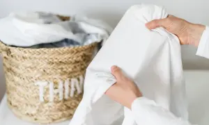 Mani che piegano un lenzuolo bianco, vicino a un cesto di vimini con biancheria. Speriamo non ci siano macchie candeggina!