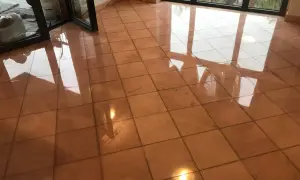 Pavimento in cotto lucido, riflessi di luce e finestre. Si intravede un secchio e sacchi, forse per pulire marmo con aceto.