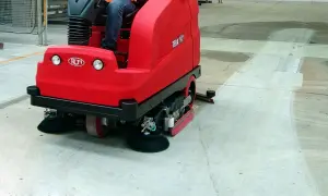 Macchina rossa per pulire pavimento in cemento in azione, lasciando una scia pulita.