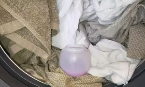 Un cestello pieno di biancheria, con un misurino di ammorbidente rosa. Si può mettere l'ammorbidente direttamente nel cestello per un bucato profumato.