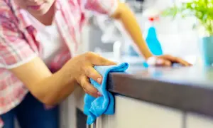 Donna pulisce il piano della cucina con un panno blu, un metodo efficace per sgrassare la cucina e mantenerla splendente.