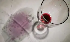 Un bicchiere rovesciato ha lasciato macchie di vino rosso sui capi colorati di una tovaglia.