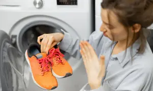 Donna con espressione disgustata tiene in mano scarpe da ginnastica arancioni, pronte per essere lavate in lavatrice.