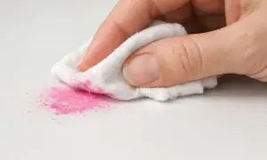 Mano che pulisce polvere rosa da superficie bianca con panno. Scopri come togliere lo smalto dal pavimento in gres.