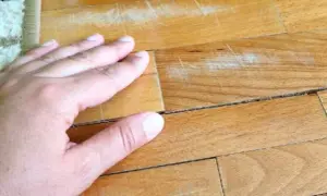 Mano sul parquet con macchie vecchie di olio e graffi evidenti.