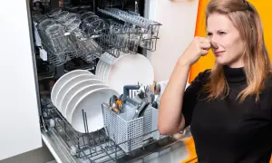 Donna tappa il naso davanti a una lavastoviglie piena di piatti, suggerendo la necessità di una cura lavastoviglie fai da te per eliminare i cattivi odori.