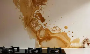 Macchie di olio sul muro della cucina, con gocce e schizzi che creano un disegno astratto sopra il piano cottura a gas.