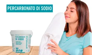 Donna annusa un asciugamano bianco fresco, accanto a un contenitore di percarbonato di sodio. Il percarbonato si può usare sui colorati per un bucato impeccabile.