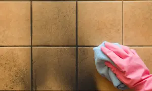 Mano con guanto rosa pulisce con panno azzurro la fuliggine dal pavimento di piastrelle marroni.