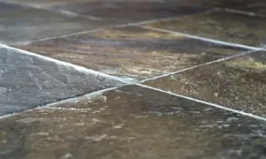 Primo piano di una pavimentazione in pietra di lavagna, con le sue venature naturali e le fughe bianche che creano un motivo geometrico.