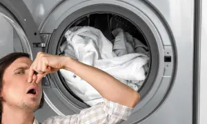 Uomo con mano sul naso davanti a un'asciugatrice che puzza, piena di biancheria umida.