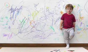 Bambino vicino a un muro pieno di scarabocchi colorati. Come togliere macchie dal muro colorato dopo il suo capolavoro.