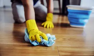 Mani con guanti gialli puliscono il pavimento in legno, rimuovendo la muffa con un panno.