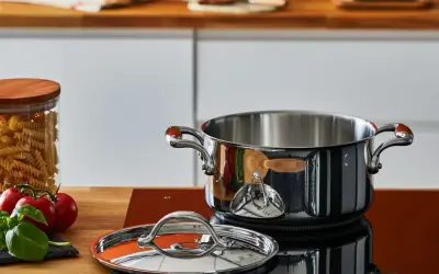 Pentola in acciaio lucido, coperchio e ingredienti freschi sul piano cottura. Scopri come pulire le pentole in acciaio per mantenerle splendenti.