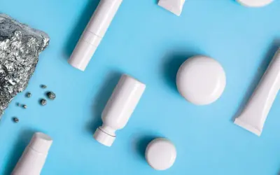 Pietra grezza e piccoli frammenti metallici accanto a flaconi e tubetti bianchi, evocano la purezza dei cosmetici nichel free.