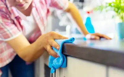 Donna pulisce il piano della cucina con un panno blu, un metodo efficace per sgrassare la cucina e mantenerla splendente.