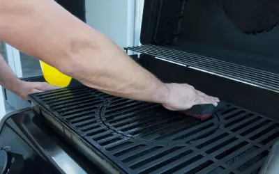 Uomo pulisce la griglia della barbecue con una spugna. Un liquido giallo viene versato da un contenitore.