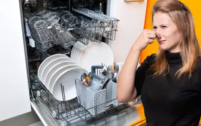Donna tappa il naso davanti a una lavastoviglie piena di piatti, suggerendo la necessità di una cura lavastoviglie fai da te per eliminare i cattivi odori.