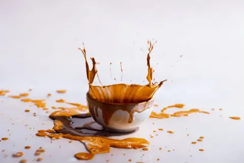 Un caffè schizza da una tazza, creando un'onda liquida. Le macchie di caffè vanno via, lasciando una scia dorata sulla superficie bianca.