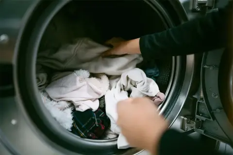 Mani che caricano la lavatrice con vestiti chiari. Speriamo che l'ammorbidente non lasci macchie sui vestiti.