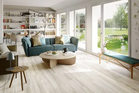 Soggiorno luminoso con divano blu e pavimento in gres porcellanato effetto legno, che mostra come rendere lucido il gres porcellanato effetto legno.
