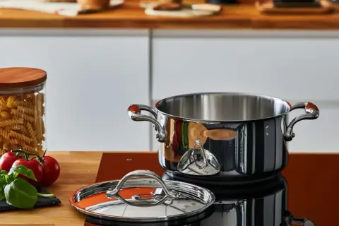 Pentola in acciaio lucido, coperchio e ingredienti freschi sul piano cottura. Scopri come pulire le pentole in acciaio per mantenerle splendenti.