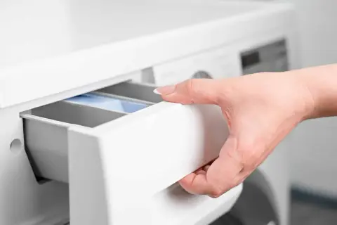 Mano inserisce cassetto lavatrice con percarbonato e candeggina.