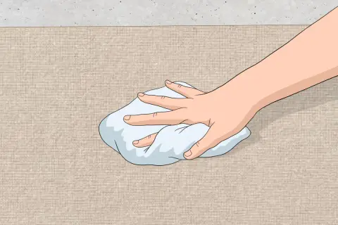 Mano che tampona una macchia su tessuto beige con un panno bianco. Guida su come togliere macchia d'olio.