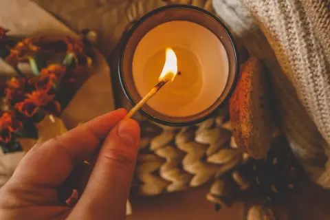 Un fiammifero illumina una candela, un modo per spegnere le candele senza fare fumo. Atmosfera autunnale con fiori e zucca.
