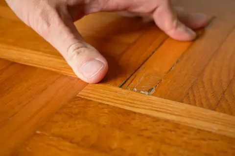 Dito come togliere la cera dal parquet verniciato: un dito indica una crepa sul legno lucido, mostrando il problema.