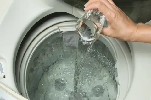 Mano versa liquido da un bicchiere nella lavatrice. Scopri quale aceto per lavatrice usare per un bucato impeccabile.