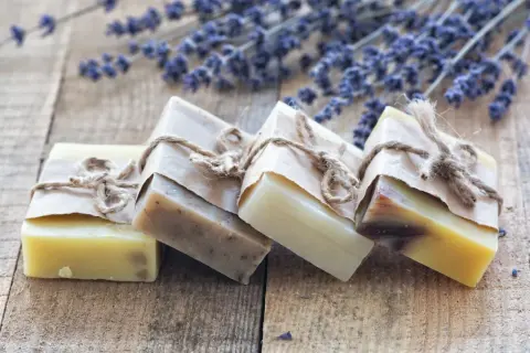 Saponi ecologici artigianali, avvolti in carta e legati con spago, su un tavolo di legno con fiori di lavanda.