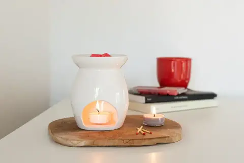 Diffusore bianco con candela accesa e cubetti di cera profumata sopra. Un'altra candela e fiammiferi completano la scena, mostrando che cos'è la cera per profumare l'ambiente.