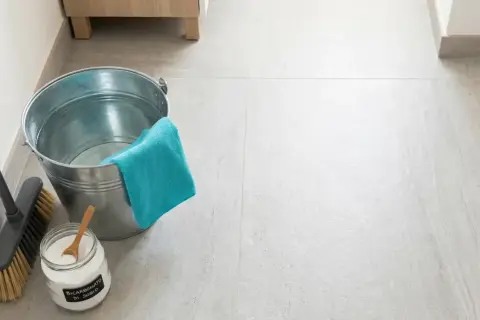 Secchio, scopa e barattolo di bicarbonato per pavimenti, pronti per una pulizia profonda.