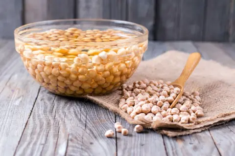 Ceci sono ceci in ammollo tutta la notte in una ciotola di vetro. Accanto, ceci secchi su tela grezza con un cucchiaio di legno.