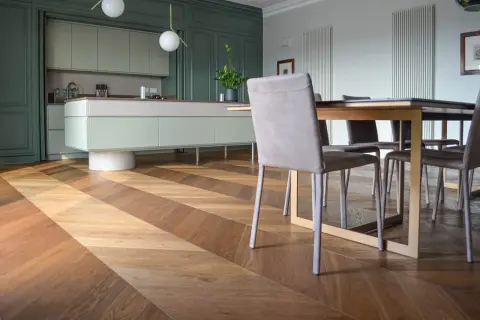 Un elegante parquet a spina di pesce in legno crea un motivo a zig-zag, che si estende dalla cucina moderna alla zona pranzo.