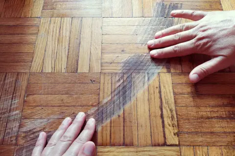 Mani sul parquet rovinato, graffi e segni evidenti. Si cerca una soluzione per pulire e ripristinare il legno.