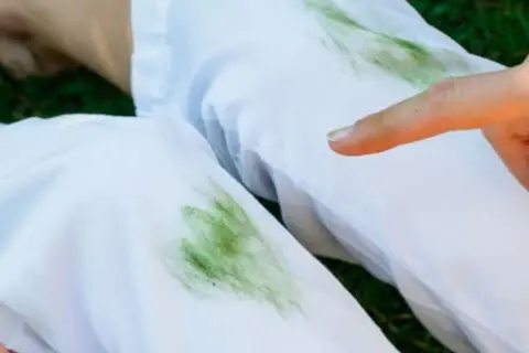 Un dito indica delle macchie d'erba su pantaloni bianchi, un piccolo disastro dopo una giornata all'aperto.