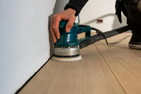 Mano che usa una levigatrice per levigare parquet a mano, creando una superficie liscia e pronta per la finitura.